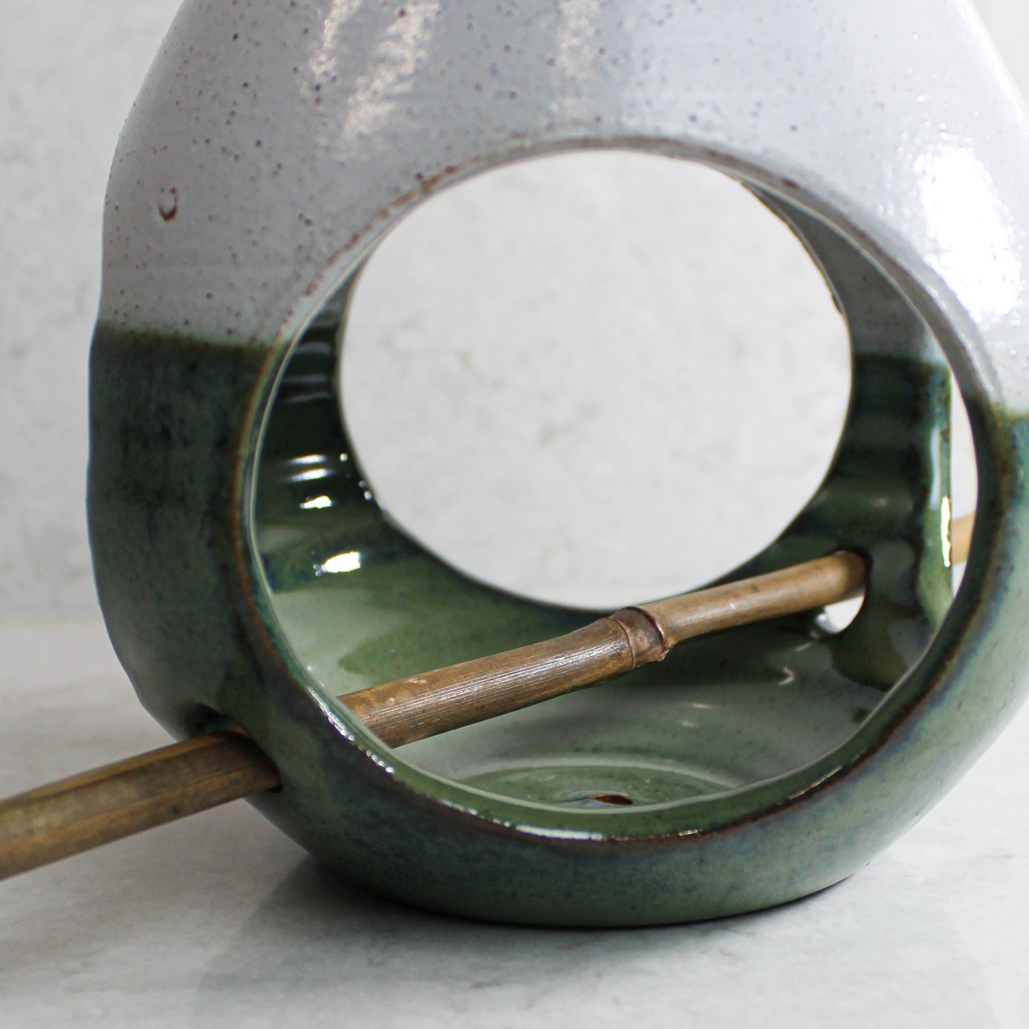 Close up of inside of pottery green and white bird feeder with bamboo perch 