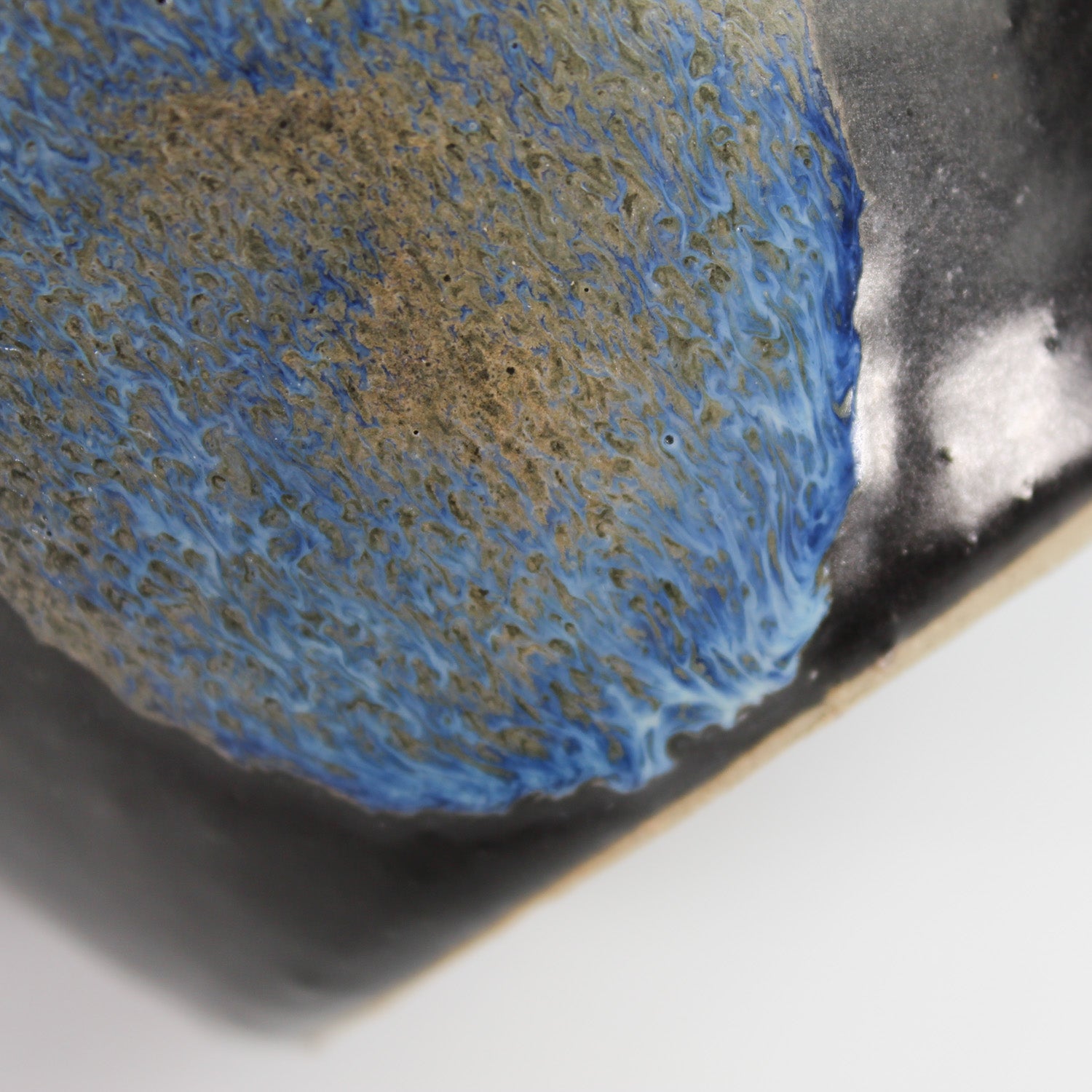 Close up of blue detailing on small black ceramic vase