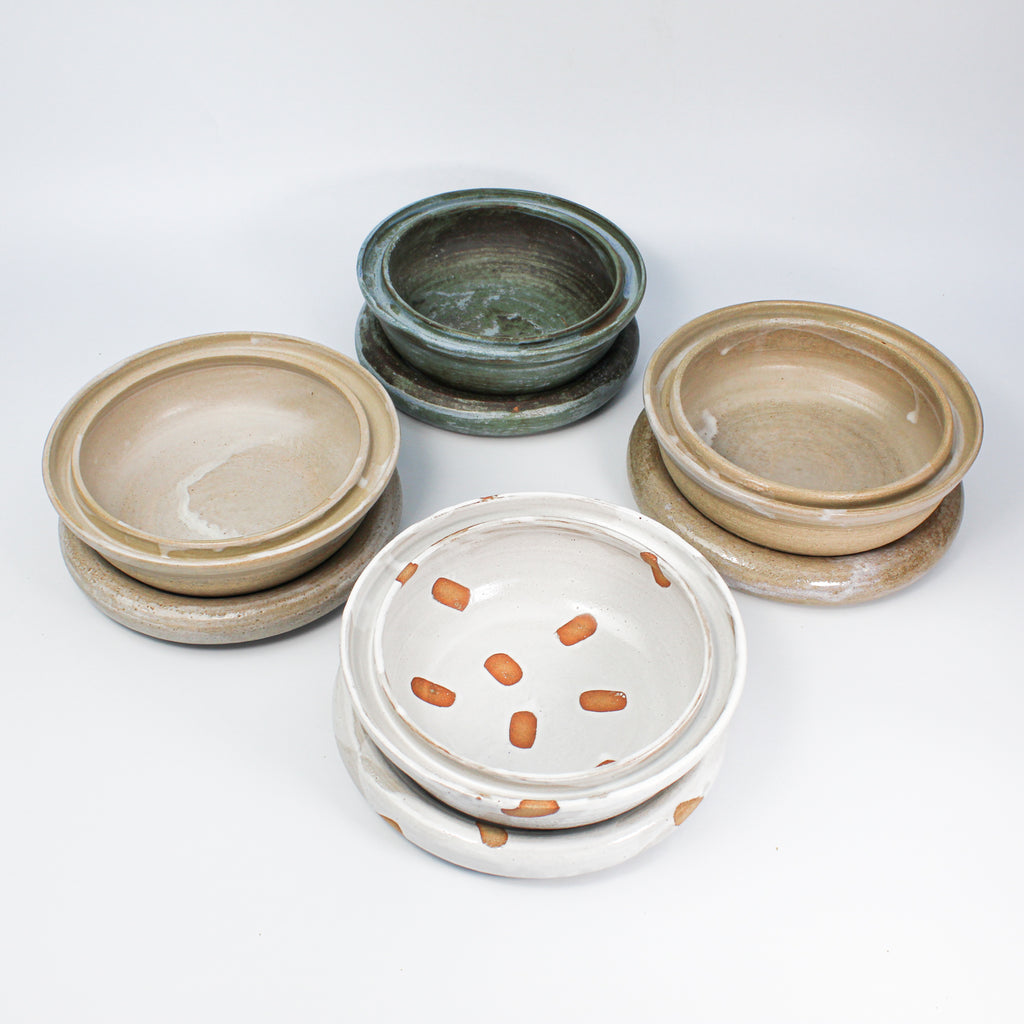 Set of four pottery dog food and water bowls. One in blue, one in natural gloss, one in natural matt and one in white spotted.