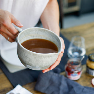 Hand holding grey glazed pottery gravy jug with gravy inside 