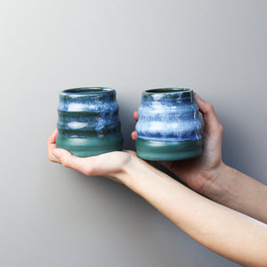 Hands holding a pair of green and blue mini pottery wobble vases 