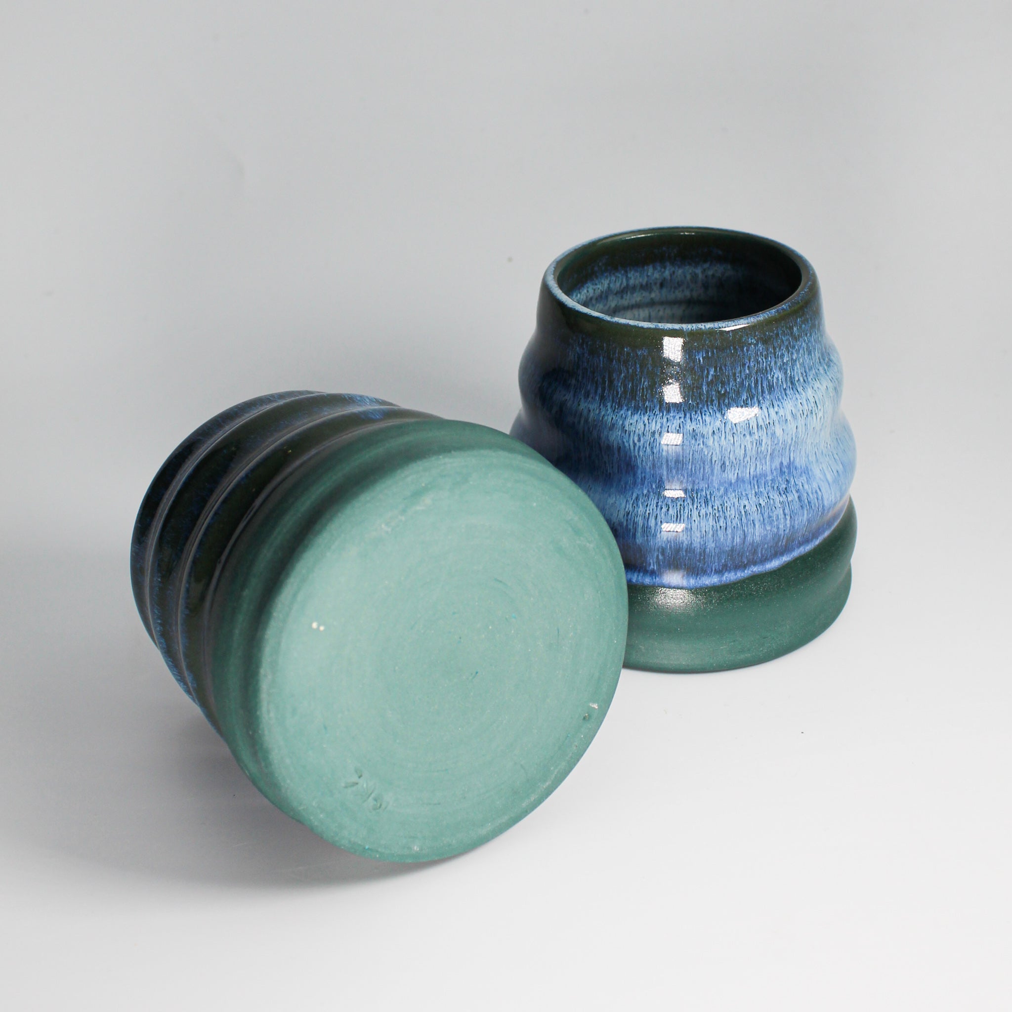 Pair of blue and green pottery mini wobble vases. One is lying on its side so you can see the bottom of the vase 