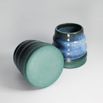 Load image into Gallery viewer, Pair of blue and green pottery mini wobble vases. One is lying on its side so you can see the bottom of the vase 
