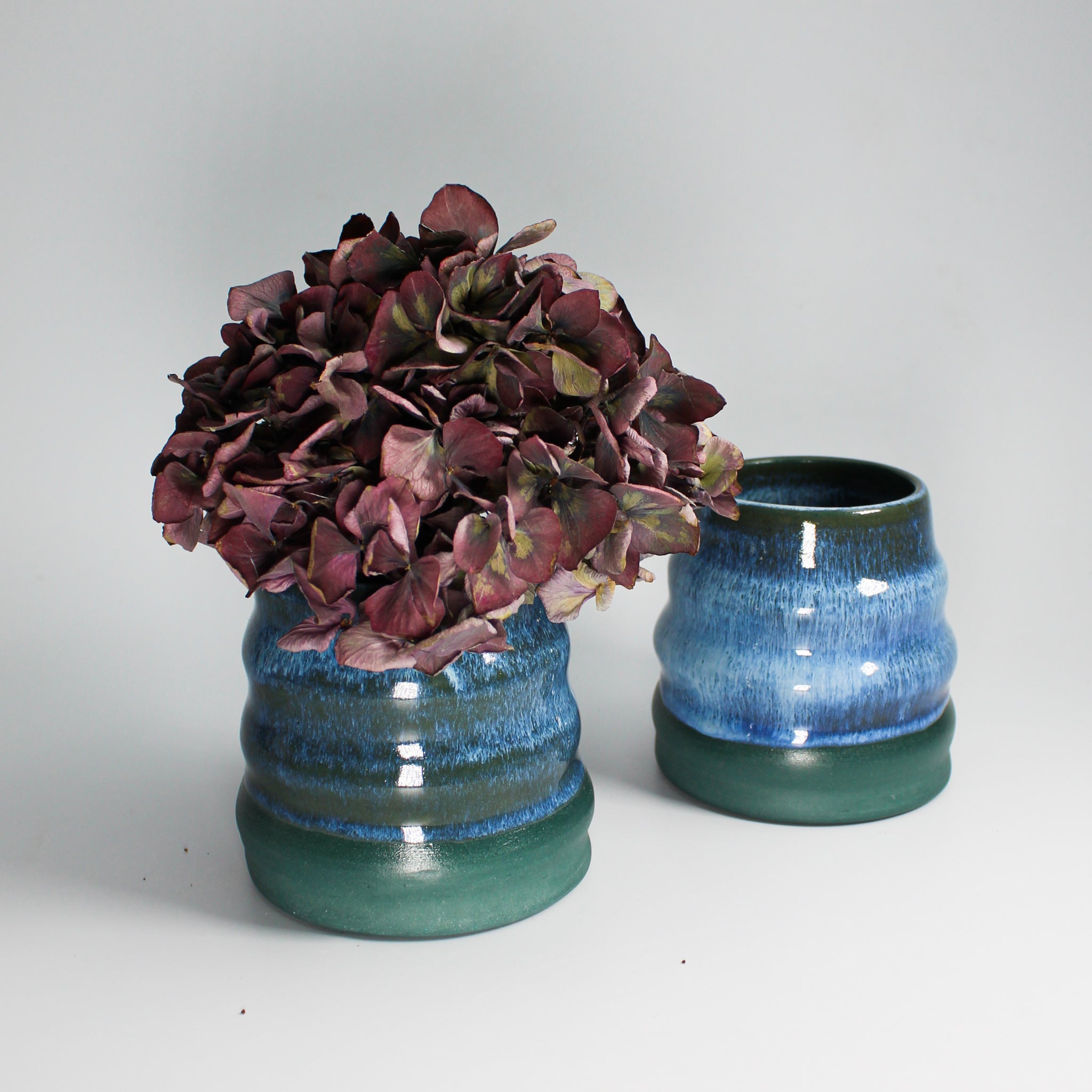 Pair of blue and green pottery mini wobble vases. One has dried flowers in.