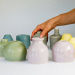 Load image into Gallery viewer, Hand picking up a small grey pottery bud vases from a collection 
