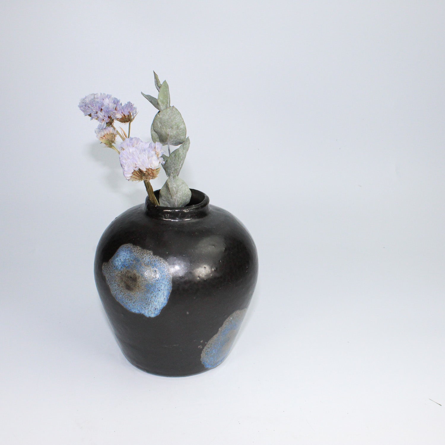 Small black ceramic vase with blue detailing and dried flowers,